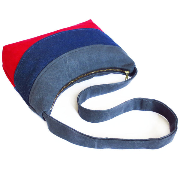 the holland everyday bag is gray, blue, and red, with a black brass zipper